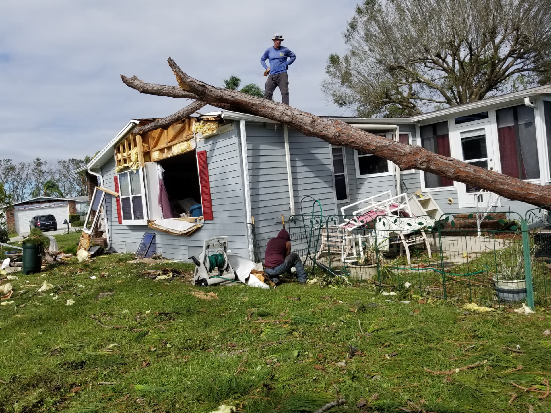 Crew member on the roof of a manufactured home with a large pine tree fallen across it after Hurricane Ian